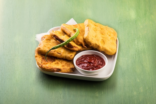 Pane Pakora o pakoda servito con ketchup, peperoncino verde e fette di cipolla, popolare spuntino indiano all'ora del tè. Messa a fuoco selettiva