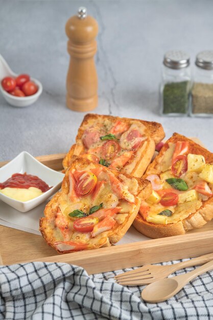 Pane per pizza condito con bastoncini di gamberi, pomodori, salsiccia, formaggio, in un vassoio di legno