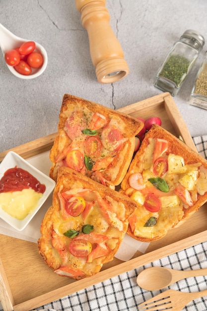 Pane per pizza condito con bastoncini di gamberi, pomodori, salsiccia, formaggio, in un vassoio di legno