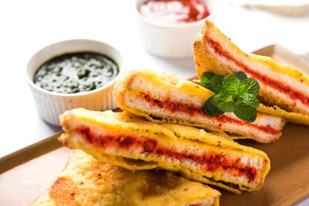 Pane sandwich Pakora o pakoda (forma di triangolo) servito con ketchup di pomodoro, chutney, peperoncino verde e fette di cipolla, popolare snack indiano all'ora del tè. Messa a fuoco selettiva