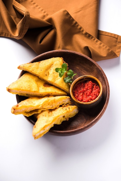 Pane sandwich Pakora o pakoda (forma di triangolo) servito con ketchup di pomodoro, chutney, peperoncino verde e fette di cipolla, popolare snack indiano all'ora del tè. Messa a fuoco selettiva