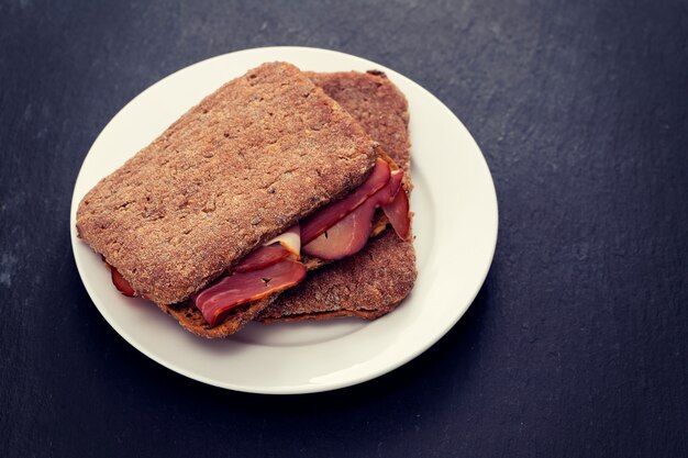 Pane scuro con carne affumicata sul piatto bianco