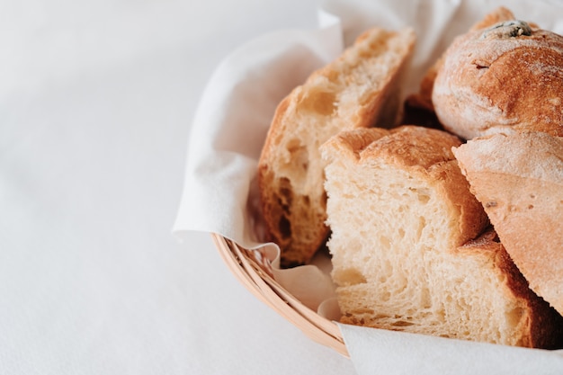 Pane semplice e pane all'uvetta posti in un cestino di vimini su un tavolo con una tovaglia bianca