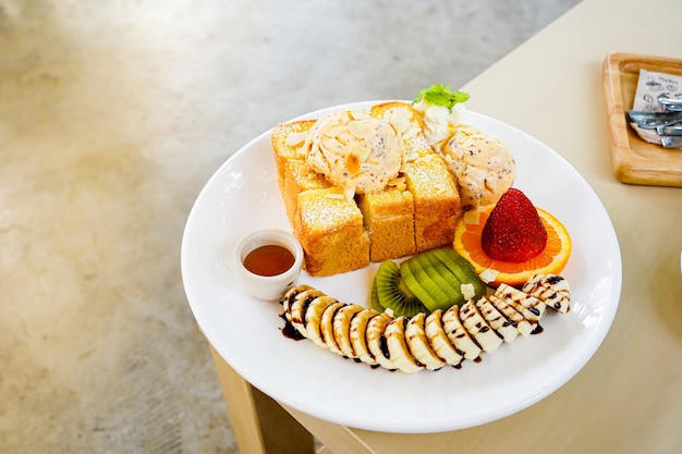 pane tostato al miele servito con frutta mista, banana a fette, gelato e guarnito con fetta di mandorle e sciroppo di miele