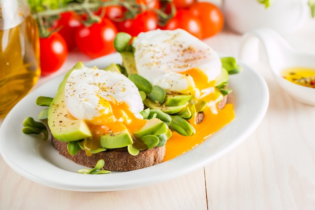 Pane tostato con avocado, pomodorini e uova in camicia su fondo di legno. Colazione con cibo vegetariano, concetto di dieta sana.