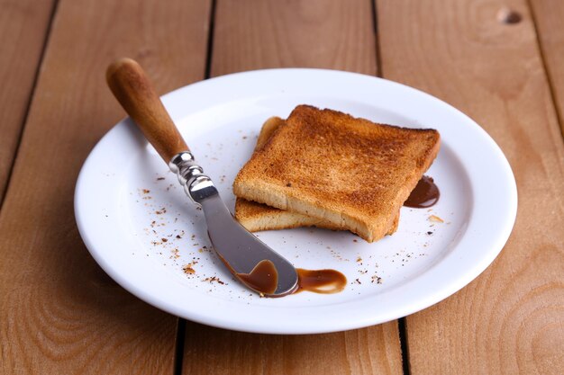 Pane tostato con cioccolato su piatto con coltello sullo sfondo di tavolo in legno