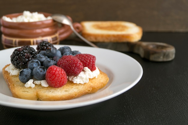 Pane tostato con ricotta e frutti di bosco freschi.