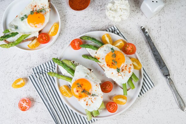 Pane tostato croccante con crema di formaggio cremoso, uovo fritto e asparagi in un piatto su uno sfondo bianco.