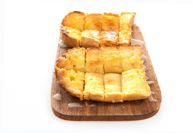 Pane tostato e latte condensato sul piatto di legno su sfondo bianco