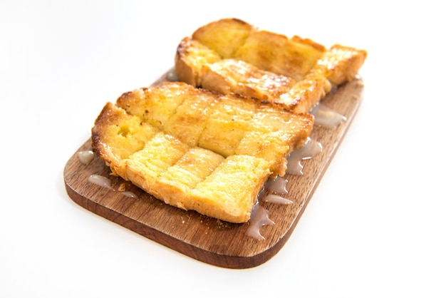 Pane tostato e latte condensato sul piatto di legno su sfondo bianco