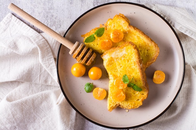 Pane tostato fritto in uovo con miele di physalis e menta su un piatto Dessert fatto in casa Vista dall'alto Primo piano