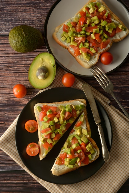 Pane tostato sano con avocado, pomodorini e formaggio su un piatto. Tavolo di legno.