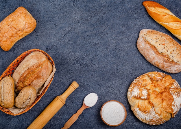 Panetteria - vari panini croccanti rustici con pane e panini, farina di grano, un mazzo di spighette su uno sfondo scuro.