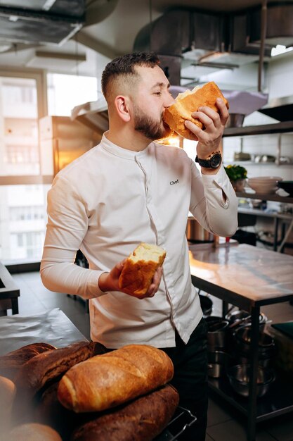 Panettiere bello in uniforme che morde il pane appena sfornato al forno