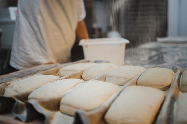 Panettiere che mette farina in polvere su pezzi di pasta di pane mentre riposano su un panno couche