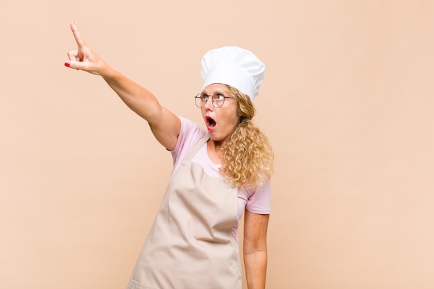 Panettiere donna di mezza età che si sente scioccato e sorpreso, indica e guarda in soggezione con sguardo stupito e a bocca aperta