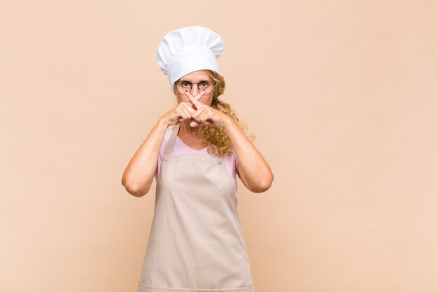 Panettiere donna di mezza età dall'aria seria e scontenta con entrambe le dita incrociate in segno di rifiuto, chiedendo silenzio