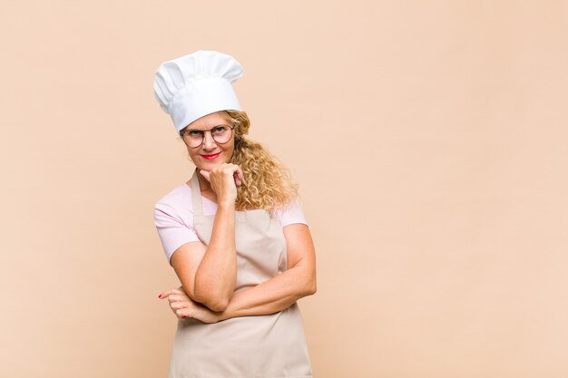 Panettiere donna di mezza età sorridente, godersi la vita, sentirsi felice, amichevole, soddisfatto e spensierato con la mano sul mento