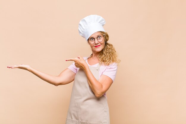 Panettiere donna di mezza età sorridente, sentendosi felice, spensierato e soddisfatto, indicando il lato