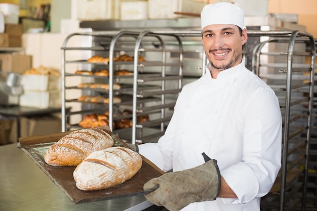 Panettiere felice che tiene vassoio di pane fresco