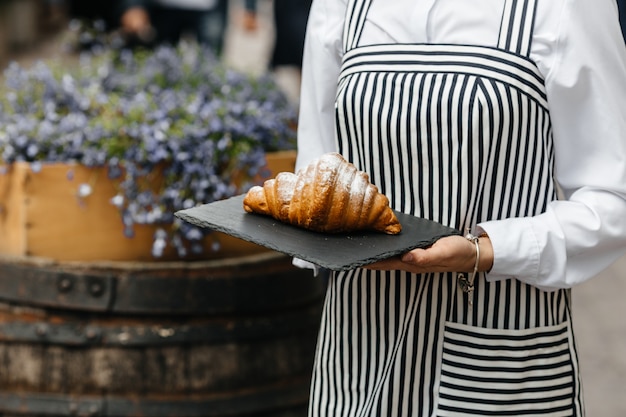 Panettiere femminile che mostra i croissant freschi deliziosi nel caffè della via