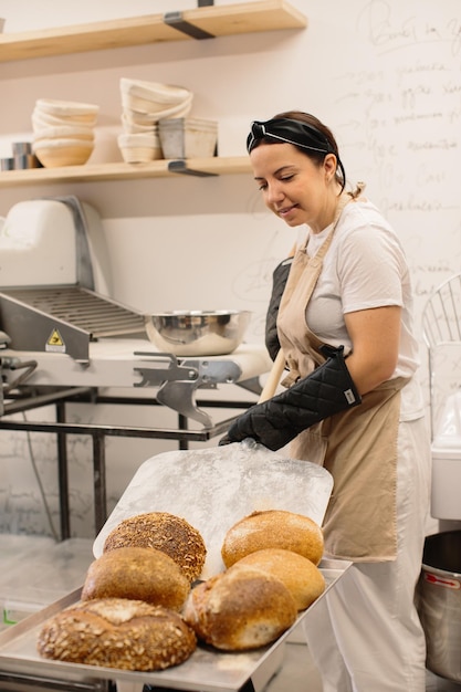 Panettiere femminile che utilizza una buccia per estrarre una pagnotta dal forno in una panetteria