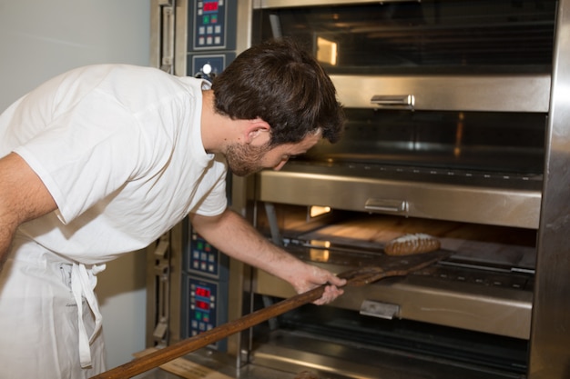 Panettiere in uniforme che toglie con pala di pane appena sfornato