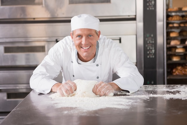 Panettiere sorridente impastare la pasta sul bancone