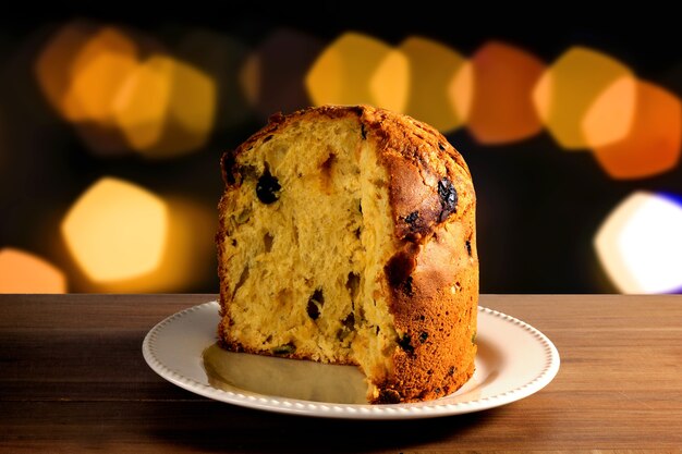 Panettone del primo piano dentro il piatto di ceramica sulla tavola di legno, fondo del bokeh con le luci,