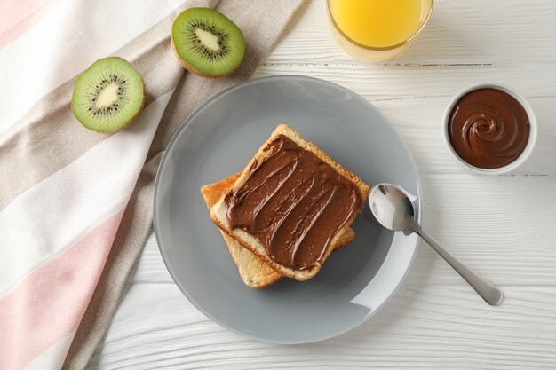 Pani tostati con la crema di choco sul piatto, sul kiwi e sul succo su fondo di legno, vista superiore