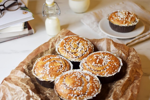 Panini alla cannella appena sfornati con codette su carta da forno. Vicino a una bottiglietta e un bicchiere di latte