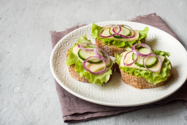 Panini aperti con formaggio, cetrioli e cipolle sul pane integrale. Messa a fuoco selettiva.