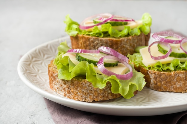 Panini aperti con formaggio, cetrioli e cipolle sul pane integrale. Messa a fuoco selettiva.