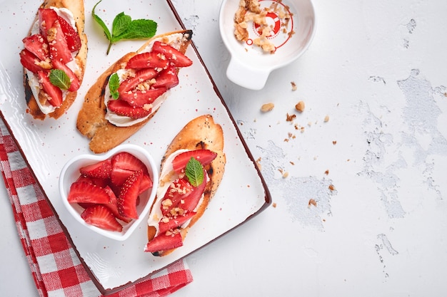 Panini aperti con fragole, formaggio morbido alla menta e noci in un piatto di ceramica su uno sfondo di pietra grigio chiaro. Estate e cibo dietetico sano, concetto di cibo vegetariano. Vista dall'alto.