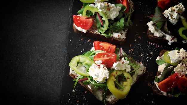 Panini aperti sani con insalata e formaggio bianco su sfondo nero.