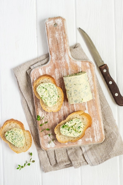 Panini con burro alle erbe sul tagliere su fondo di legno bianco.