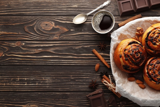 Panini con cannella e cioccolato su un fondo di legno marrone. Stecca di cannella e caffè espresso nero. Posto per il testo. Vista dall'alto.