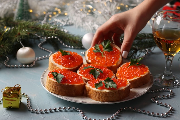 Panini con caviale rosso su un piatto contro uno sfondo azzurro. Spuntino festivo. La donna allunga la mano per togliere il panino dal piatto.