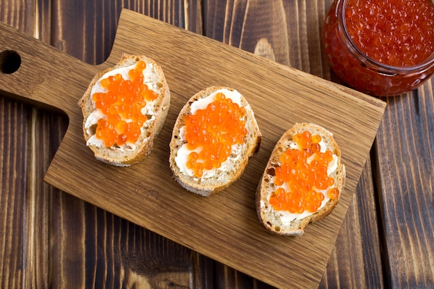 Panini con caviale rosso sul tagliere di legno. Vista dall'alto.