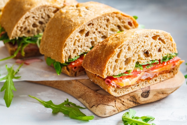 Panini con ciabatta, prosciutto e verdure su una tavola di legno