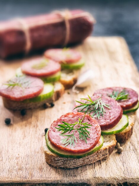 panini con pane di segale e salame di salsiccia affumicata con aneto e cetriolo sul tagliere di legno, primo piano