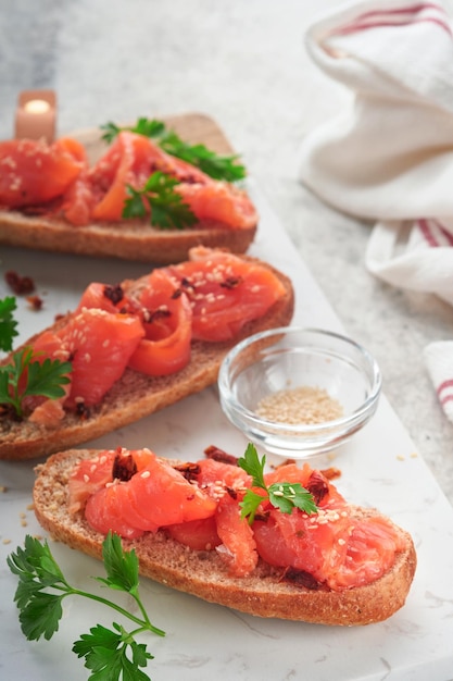 Panini con salmone salato Panini aperti con cereali o pane di segale integrale con salmone salato semi di sesamo e pomodoro secco su supporto in marmo bianco Frutti di mare Cibo sano Cucina scandinava