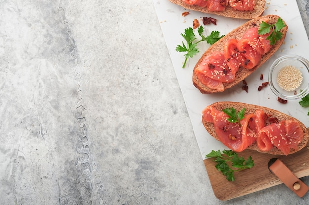 Panini con salmone salato Panini aperti con cereali o pane di segale integrale con salmone salato semi di sesamo e pomodoro secco su supporto in marmo bianco Frutti di mare Cibo sano Cucina scandinava