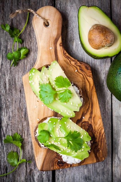 Panini con semi di sesamo avocado a fette di pane di segale e prezzemolo su tagliere di legno