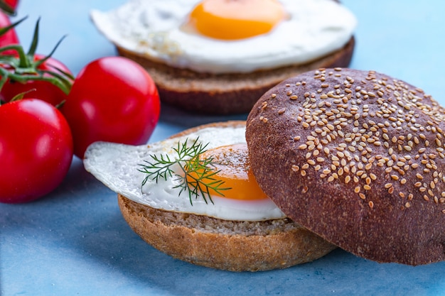 Panini con uova di gallina fatte in casa e fritte cosparse di spezie e sale per una colazione su una superficie blu. Alimento proteico. Panini con uova