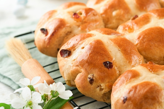 Panini crociati caldi di Pasqua Tradizionali panini crociati di Pasqua con uova di zucchero di cioccolato con fiori di ciliegio o mela su sfondi di legno leggeri rustici Pasqua