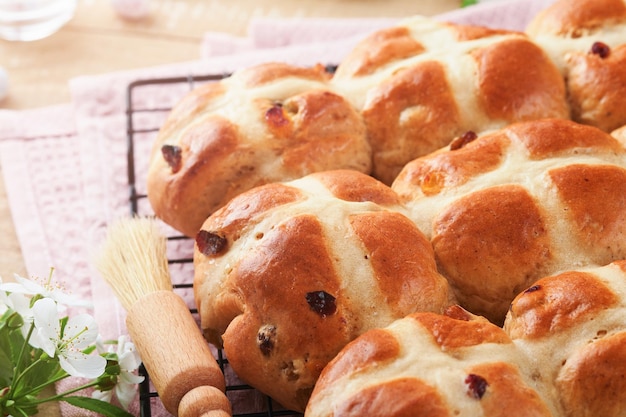 Panini crociati caldi di Pasqua Tradizionali panini crociati di Pasqua con uova di zucchero di cioccolato con fiori di ciliegio o mela su sfondi di legno leggeri rustici Pasqua