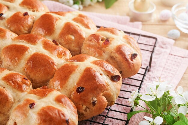 Panini crociati caldi di Pasqua Tradizionali panini crociati di Pasqua con uova di zucchero di cioccolato con fiori di ciliegio o mela su sfondi di legno leggeri rustici Pasqua