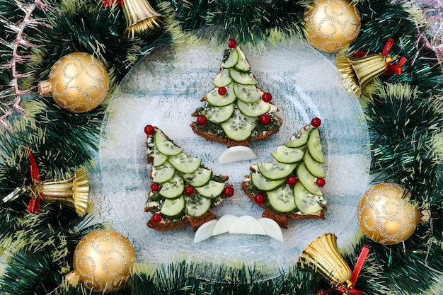 Panini di Capodanno con pane nero, formaggio e cetrioli a forma di albero di Natale, bacche decorate