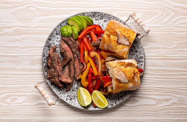 Panini Fajitas a base di piatto tradizionale messicano Fajita di manzo e pane bianco serviti con avocado maturo su fondo rustico in legno bianco dall'alto, spuntino sano cibo messicano americano